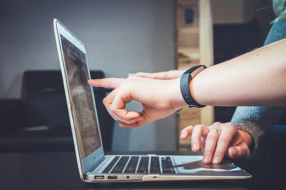 Duas pessoas a colaborar em frente a computador portátil, apontando para o ecrã durante desenvolvimento de website. Marketing Digital