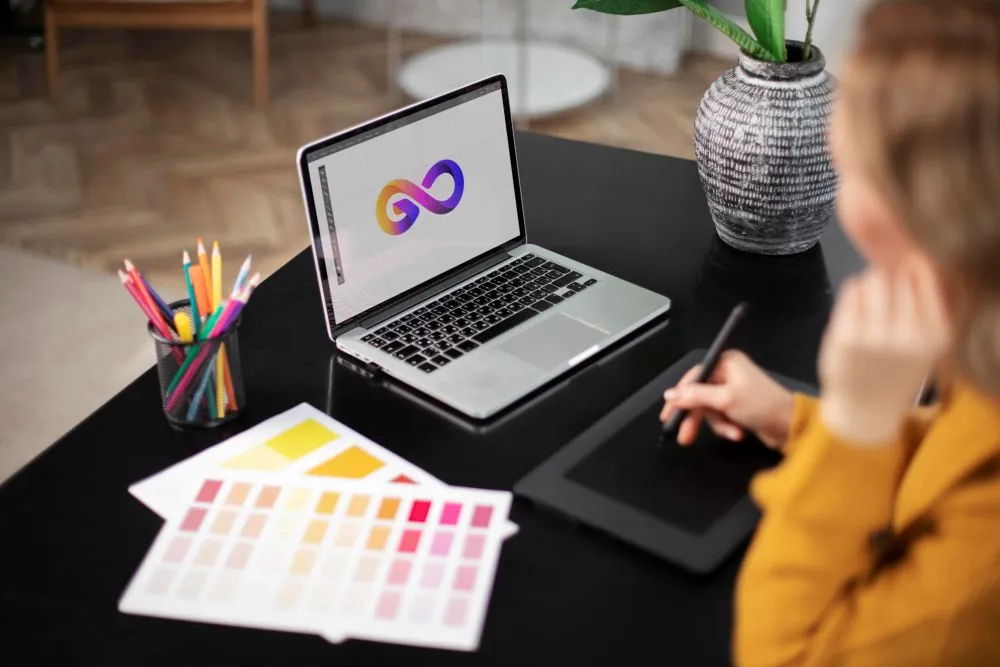 Designer gráfico a criar logótipo em computador portátil com tablet gráfico e paletas de cores